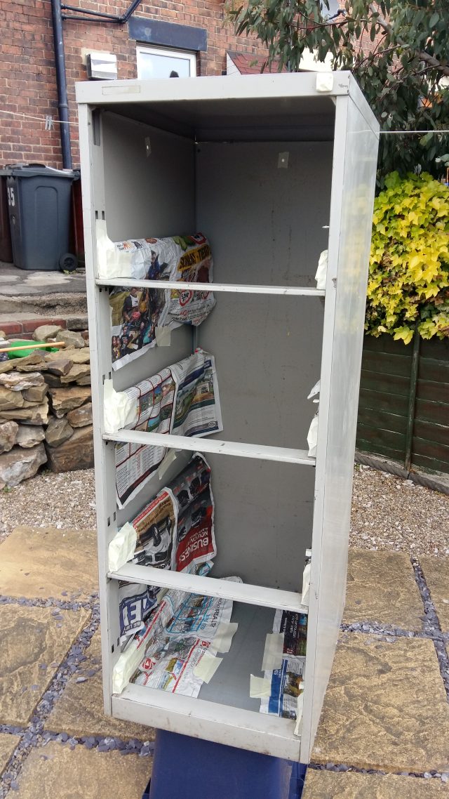 Image of a four-drawer filing cabinet, with the drawers removed. It is placed on an upturned plastic tub and has newspaper covering the internal drawer runners.