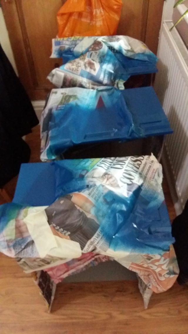 An image of three filing cabinet drawers, masked up in newspaper, with blue spray pain.