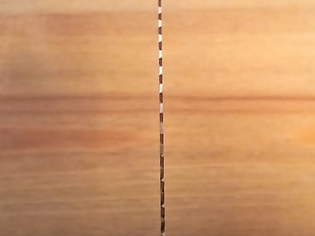 Image shows the tooth edge a Kugihiki ZETSAW replacement blade, face on. This is to show that the blade has no set to the teeth. Shown on a wooden background.