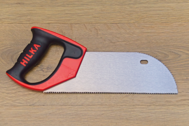 Image of a small floorboard saw, with a soft-grip D-handle and saw teeth on the rounded nose. Shown on a wooden background.