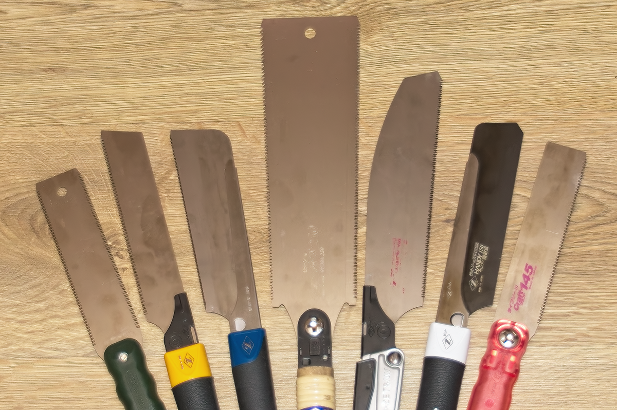 Seven different Japanese Saws (nokogiri) displayed in a fan shape and shown on a wooden background.