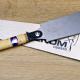 A Ryoba-noko Japanese Saw placed over a Western First Fix handsaw in a cross, shown on a wooden background.