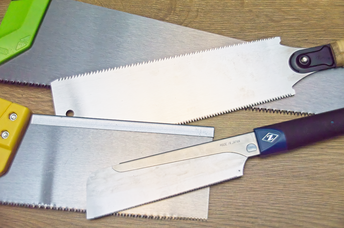 A close-up of four saws. Two Western saws are on the left of the image. Two Japanese Saws are on the right of the image. Shown on a wooden background.